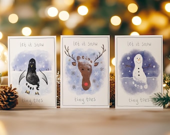 May include: Three Christmas cards with watercolor illustrations. One features a penguin, another a reindeer, and the last a snowman, all created with footprints. Each card has the text "Let it snow" and "tiny toes".