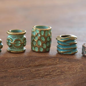 Könnte beinhalten: Fünf verschiedene Metallperlen mit komplizierten Designs. Die Perlen sind in einem Mix aus Grün und Gold gehalten und haben einen abgenutzten, antiken Look.