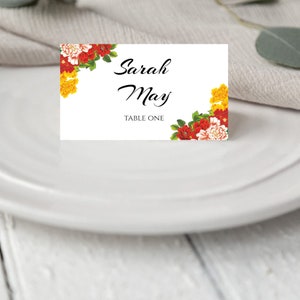 Pode incluir: Cart&atilde;o de lugar branco com borda floral com flores vermelhas, amarelas e brancas. O texto diz "Sarah May, Mesa Um."