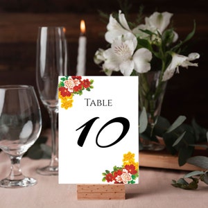 Pode incluir: Cart&atilde;o de n&uacute;mero de mesa branco com design floral vermelho, amarelo e verde. O cart&atilde;o diz "TABLE 10" em texto preto.
