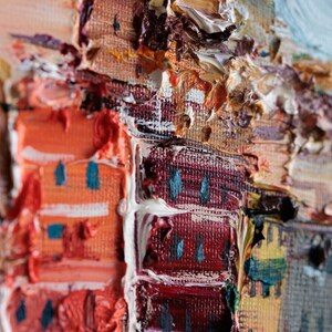 May include: Close-up of an oil painting showing a cityscape with textured brushstrokes. The artwork features buildings in shades of orange, red, and grey, with accents of blue and white. The painting style is impressionistic.