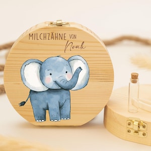Könnte beinhalten: Eine hölzerne Zahnfee-Box mit einer blauen Elefanten-Illustration und dem Text "MILCHZÄHNE VON Noah". Die Box hat einen Klappdeckel und ein kleines Glasfläschchen mit einem Korkverschluss.
