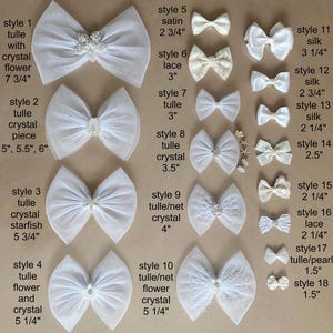 Puede incluir: Una colección de dieciocho lazos blancos para el cabello en varios estilos, incluyendo tul, satén, encaje y seda. Muchos lazos presentan adornos de cristal, flores o estrellas de mar. Cada lazo está etiquetado con un número de estilo y tamaño.