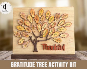 Puede incluir: Kit de actividades de árbol de gratitud de madera con un diseño de árbol marrón y etiquetas en forma de hoja. Las etiquetas están inscritas con palabras como "familia", "escuela" y "amigos". La palabra "Thankful" se muestra en letras naranjas. El kit está sobre una base de madera.