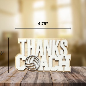 May include: A wooden sign that says "THANKS COACH" with a volleyball graphic. The sign is 4.75 inches wide and 3 inches tall. The text and volleyball are white, and the background is a light wood color.