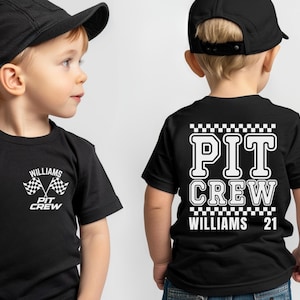 Op de afbeelding: Twee kinderen dragen zwarte T-shirts met witte tekst en geruite vlaggen. De tekst op de shirts zegt "PIT CREW" en "WILLIAMS 21".