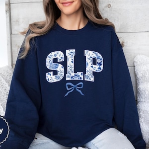 Peut inclure: Sweat-shirt bleu marine avec un motif floral blanc qui épelle "SLP" avec un nœud bleu en dessous.