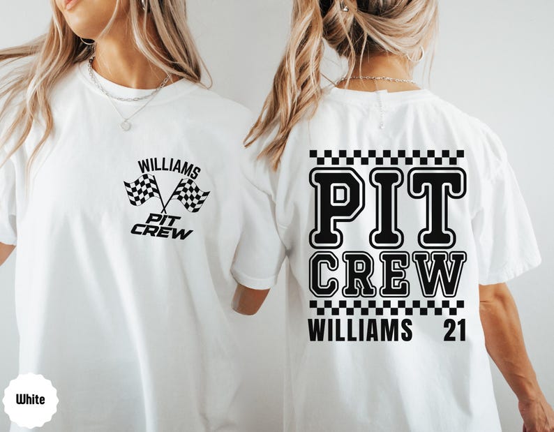 Op de afbeelding: Wit T-shirt met zwarte tekst en een geruit patroon. De tekst luidt "PIT CREW WILLIAMS 21" en "WILLIAMS PIT CREW" met een geruite vlaggrafiek.
