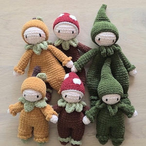 May include: A collection of five handmade crochet dolls featuring soft yarn textures. The dolls include two yellow pumpkin-themed figures, two red mushroom-capped figures, and one tall green elf-like figure with a pointed hat and ruffled collar.