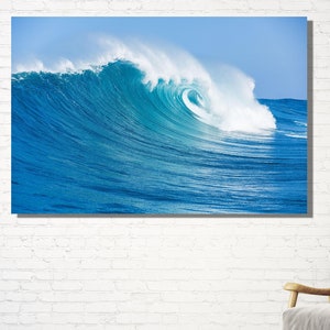 Może przedstawiać: Duża, niebieska fala oceaniczna rozbijająca się i zwijająca nad sobą. Fala rozbija się w środku obrazu, z białą pianą na szczycie.