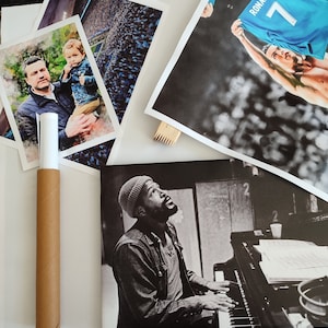 May include: A collection of three framed posters. The first poster features a black and white photo of a man playing a piano. The second poster features a photo of a man holding up a blue soccer jersey with the name "RONALDO" and the number "7" on it. The third poster features a watercolor painting of a man and a child.