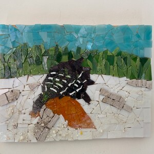 以下が含まれることがあります： 黒と白の羽根を持つ鳥がオレンジ色の葉のついた枝に止まっているモザイクアート作品。背景は青い空と緑の葉で構成されています。