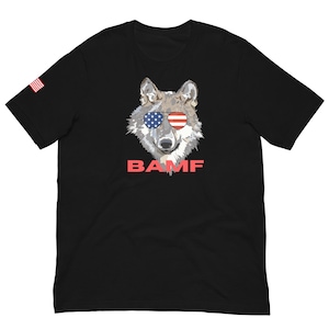 Puede incluir: Camiseta negra con un lobo que lleva gafas de sol con un diseño de bandera estadounidense. El texto "BAMF" está impreso debajo del lobo.