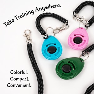May include: A selection of dog training clickers in blue, pink, and green. Each clicker features a black button and is connected to a black coiled lanyard with a silver clip. Text reads: Take Training Anywhere. Colorful, Compact, Convenient.
