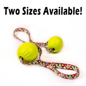 May include: Two yellow rubber dog toys with a floral patterned strap. The strap is attached to the toys and can be used to throw the toys.