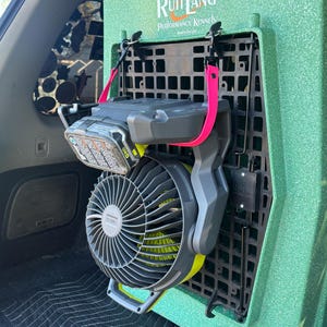 May include: A green Ruff Land Performance Kennels dog crate with a black interior, a grey fan, and a battery pack attached. The fan has grey blades and a yellow accent. A pink strap secures the fan to the crate.