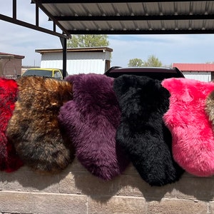 Pu&ograve; includere: Una fila di 12 coprisedia in pelliccia sintetica di vari colori, tra cui blu, grigio, bianco, rosso, marrone, viola, nero, rosa, beige e blu navy. Le coprisedia sono appese a un muro di mattoni.