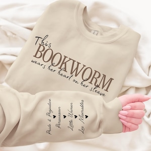 May include: Cream-colored sweatshirt with the text "This Bookworm wears her heart on her sleeve." The sleeve features the titles "Pride & Prejudice," "Persuasion," "Little Women," and "Les Miserables."