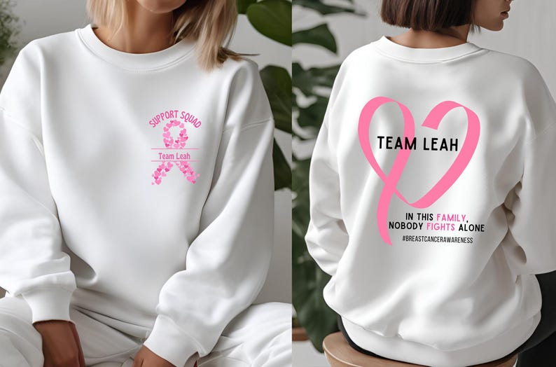Peut inclure: Sweat-shirt blanc avec des graphiques de ruban rose. Le devant pr&eacute;sente "Support Squad" et "Team Leah" avec un motif de ruban. Le dos affiche un grand c&oelig;ur de ruban rose avec "Team Leah" et le texte "In this family, nobody fights alone." #breastcancerawareness