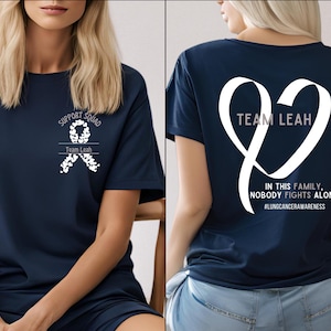 May include: Navy blue t-shirt with white text and a ribbon design. The front of the shirt says "SUPPORT SQUAD" and "Team Leah". The back of the shirt says "TEAM LEAH" and "IN THIS FAMILY, NOBODY FIGHTS ALONE" with the hashtag #LUNGCANCERAWARENESS.