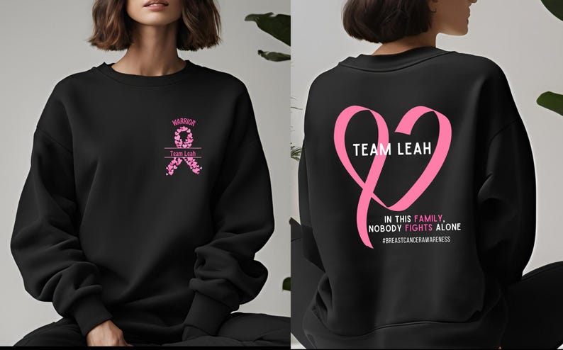 Peut inclure: Sweat-shirt noir avec un motif de ruban rose et du texte. L'avant pr&eacute;sente un ruban avec le mot "Warrior" et "Team Leah". Le dos a un ruban en forme de c&oelig;ur rose avec le texte "Team Leah" et "In this family, nobody fights alone".