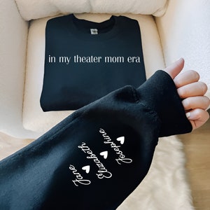 May include: Black sweatshirt with the text "in my theater mom era" on the front and the names "Jane", "Elizabeth", and "Josephine" with hearts on the sleeve.