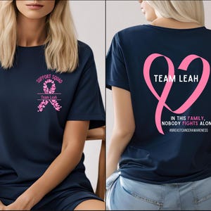 Peut inclure: T-shirt bleu marine avec texte et graphiques roses. Le devant du t-shirt indique "SUPPORT SQUAD" et "Team Leah" avec un motif de ruban rose. Le dos du t-shirt pr&eacute;sente un c&oelig;ur en ruban rose avec "TEAM LEAH" et le texte "IN THIS FAMILY, NOBODY FIGHTS ALONE".