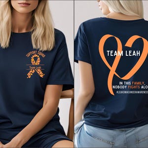 May include: Navy blue t-shirt with an orange ribbon design and the text "Support Squad Team Leah" on the front. The back of the shirt has a large orange heart with the text "Team Leah" and the text "In this family, nobody fights alone #LeukemiaCancerAwareness".
