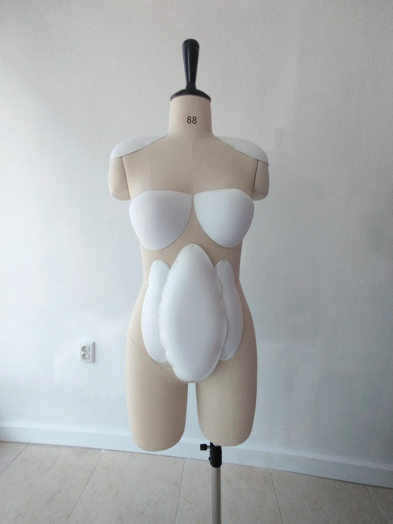 May include: A beige dress form with white padding for the shoulders, bust, and abdomen. The dress form has a black neck piece and is mounted on a metal stand. The number "88" is printed on the neck.