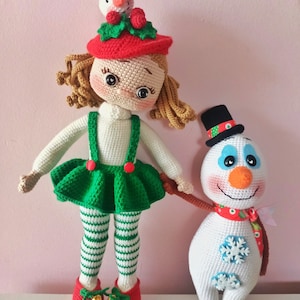 May include: A crocheted doll wearing a red and green Christmas outfit and a snowman with a black top hat and a red scarf.