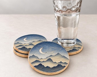 May include: A clear glass tumbler filled with water sits atop a stack of three round wooden coasters. Each coaster features a printed illustration of layered blue mountain silhouettes against a pale sky with a white crescent moon graphic.
