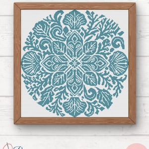 Puede incluir: Un patrón de punto de cruz enmarcado con un diseño floral turquesa y blanco. La obra de arte cuadrada presenta un patrón simétrico detallado de hojas, conchas y otros elementos botánicos. El marco es de madera marrón claro. El texto "Pura Creations" está en la esquina inferior izquierda.