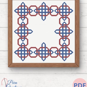 Puede incluir: Un patrón de punto de cruz enmarcado con un diseño geométrico en rojo y azul. El patrón es una serie repetida de formas entrelazadas, creando un borde alrededor de un centro blanco. El marco es de madera.