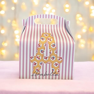 Puede incluir: Una caja de regalo a rayas rosa y blanca con una letra A floral amarilla y el nombre "Arabella" impreso en la parte delantera.