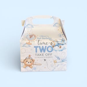 Puede incluir: Una caja blanca con forma de caballete con asa, decorada con un tema de avión en acuarela. La caja presenta un oso de peluche piloto, aviones, nubes y el texto "Oliver's 2nd Birthday, time TWO, Take Off".