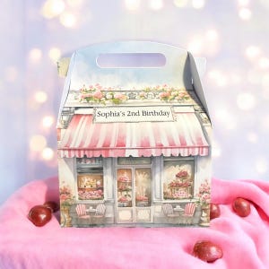 Puede incluir: Una caja de regalo blanca con un toldo a rayas rosa y blanco y un diseño floral. La caja tiene un asa y dice "Sophia's 2nd Birthday" en la parte delantera.