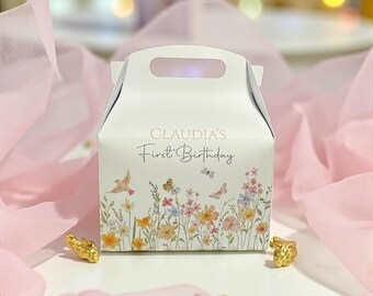 以下が含まれることがあります： 「CLAUDIA'S First Birthday」の文字が入った、白いギフトボックス。ボックスには、パステルカラーの蝶、鳥、野草のフローラルデザインが施されています。金色の装飾品がボックスの周りに配置されています。