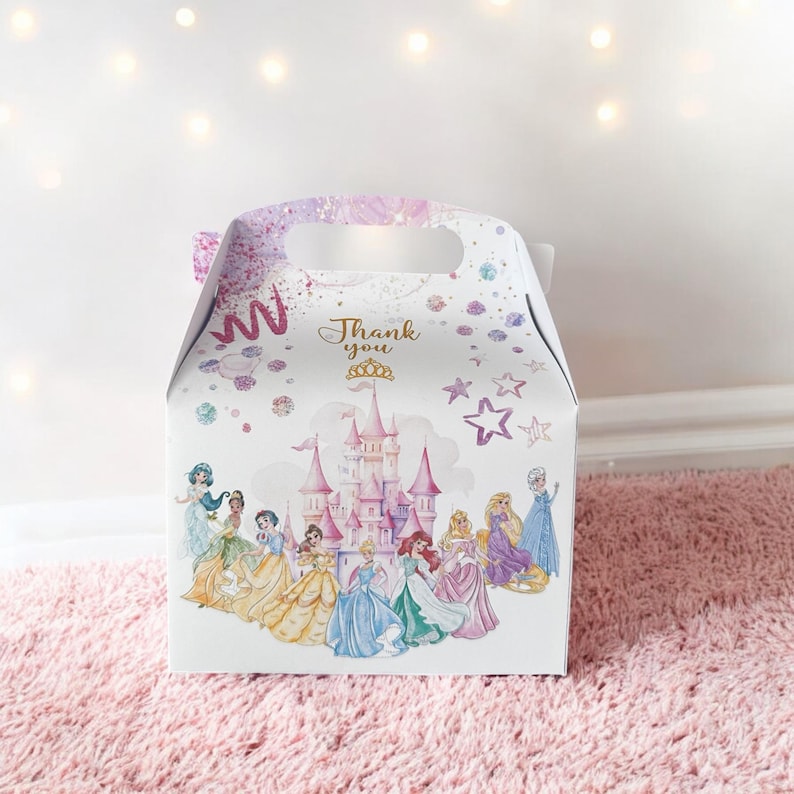 K&ouml;nnte beinhalten: Eine wei&szlig;e Geschenkbox mit einem Prinzessinnenschloss und mehreren Prinzessinnen auf der Vorderseite. Die Box hat einen Griff und sagt "Danke" mit einer goldenen Krone.