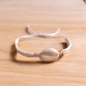 May include: White braided bracelet with a white seashell charm and clear beads.