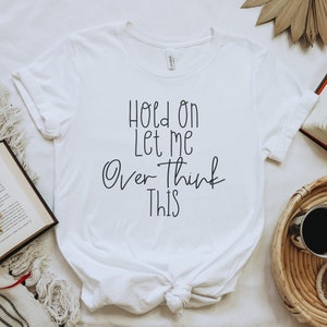 May include: White t-shirt with the text "Hold on let me over think this" written in black cursive.