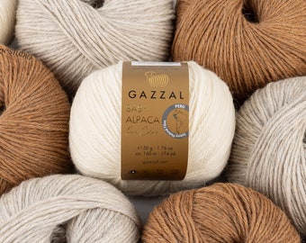 May include: A close-up of several balls of yarn in various shades of brown, beige, and white. The label on one ball reads "GAZZAL BABY ALPACA Fine Cashmere" with the weight and yardage listed.