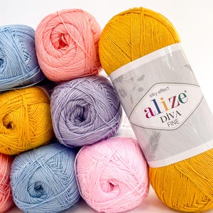 Peut inclure: Plusieurs pelotes de laine colorées en jaune, rose, bleu et violet. Une pelote de laine jaune porte une étiquette indiquant "alize DIVA FINE" avec "silky effect" au-dessus. La laine est probablement utilisée pour des projets de tricot ou de crochet.
