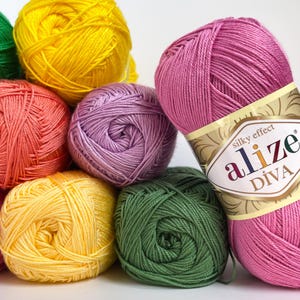 Pode incluir: Uma coleção de novelos de fios coloridos em tons de amarelo, laranja, rosa, roxo e verde. Um novelo de fio rosa tem um rótulo que diz "alize DIVA silky effect". O fio é bem enrolado e parece macio.