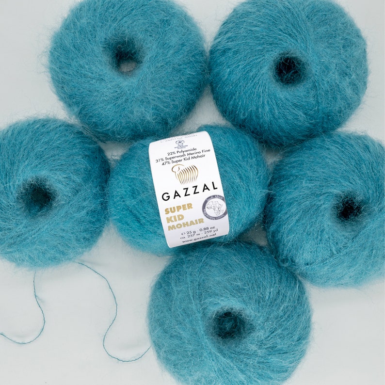 May include: Five skeins of teal blue yarn, labeled "GAZZAL SUPER KID MOHAIR" with the yarn composition: 22% Polyamide, 31% Superwash Merino Fine, 47% Super Kid Mohair. Each skein weighs 25 g (0.88 oz) and contains 225 m (247 yds) of yarn.