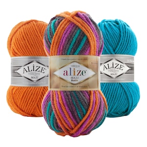 Op de afbeelding: Drie bollen Alize Superlana Maxi garen in levendige kleuren. Eén is effen oranje, een andere is een mix van oranje, paars, blauwgroen en grijs, en de derde is effen turquoise. Elke bol heeft een label met de merknaam.
