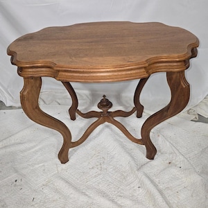 May include: A wooden side table with a scalloped edge and curved legs. The table has a light brown finish and a decorative center support. The table's dimensions are approximately 30 inches long, 20 inches wide, and 28 inches high.