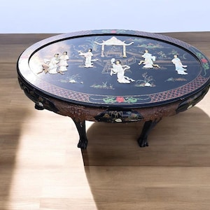 May include: A black oval coffee table with a hand-painted scene of people and a pagoda. The table top is inlaid with mother-of-pearl and has a decorative border. The table has four legs.