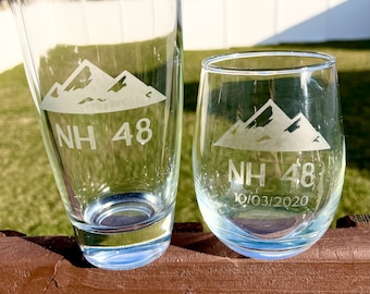 May include: Two clear glass drinking glasses with an etched design of mountains and the text "NH 48". The smaller glass has the additional text "10/03/2020".