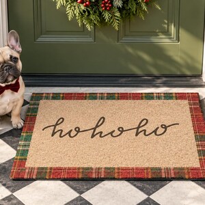 Puede incluir: Un felpudo rectangular con un centro color canela que presenta el texto negro en cursiva hohoho. La alfombra est&aacute; bordeada por un patr&oacute;n de cuadros rojos y verdes. Un bulldog franc&eacute;s de color leonado con pajarita de terciopelo rojo oscuro.