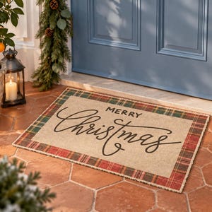 May include: A rectangular doormat with a tan center and a red, green, and white plaid border. The text Merry Christmas is printed in the center in a black script and block font. The mat is positioned on a tiled floor in front of a blue door.